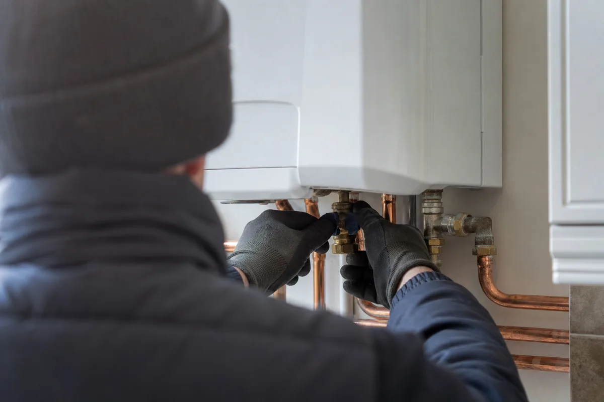 Mains d&rsquo;un technicien contrôlant la pression d&rsquo;un circuit de chauffage, lumière d&rsquo;hiver douce