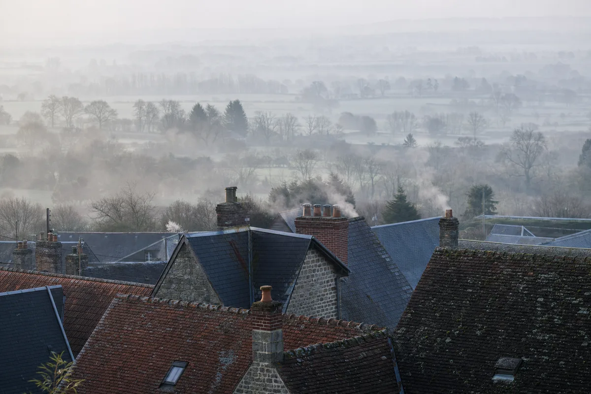 Toits d’un village normand avec cheminées fumantes un matin d’hiver
