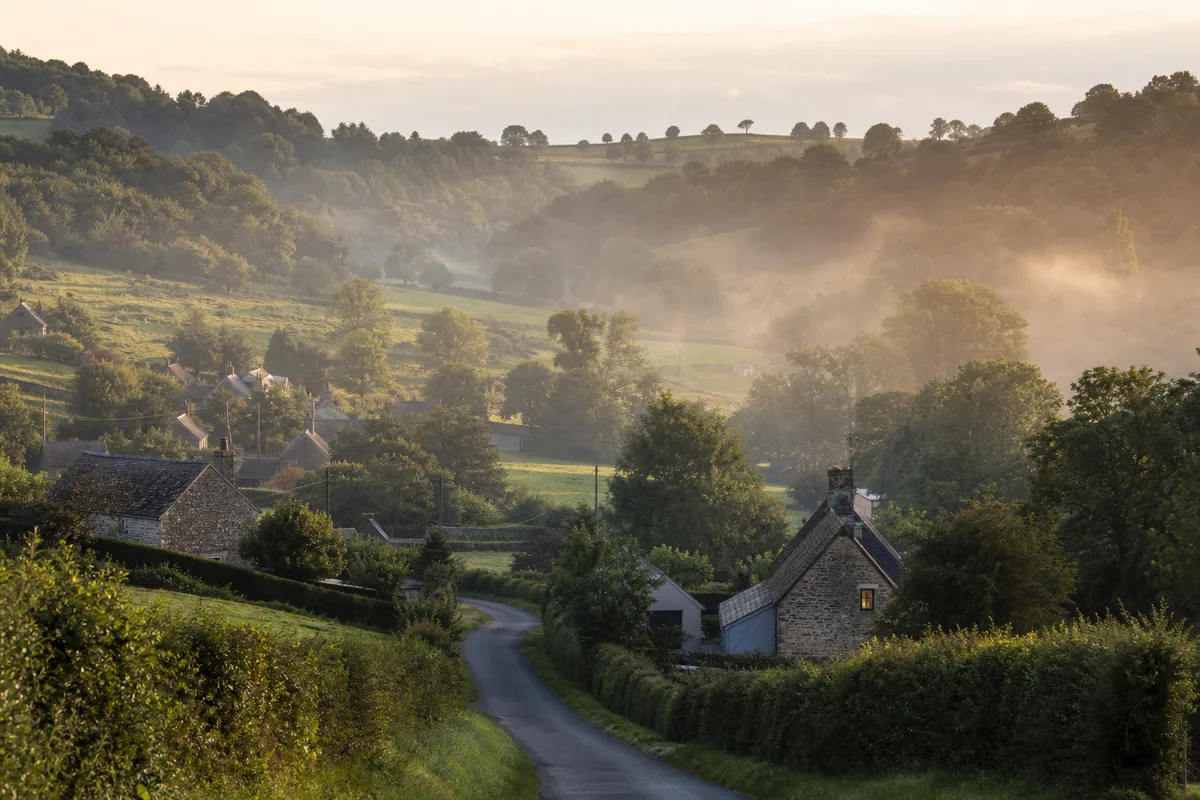 Vallée bocagère avec maisons en pierre et brume légère en fin de journée